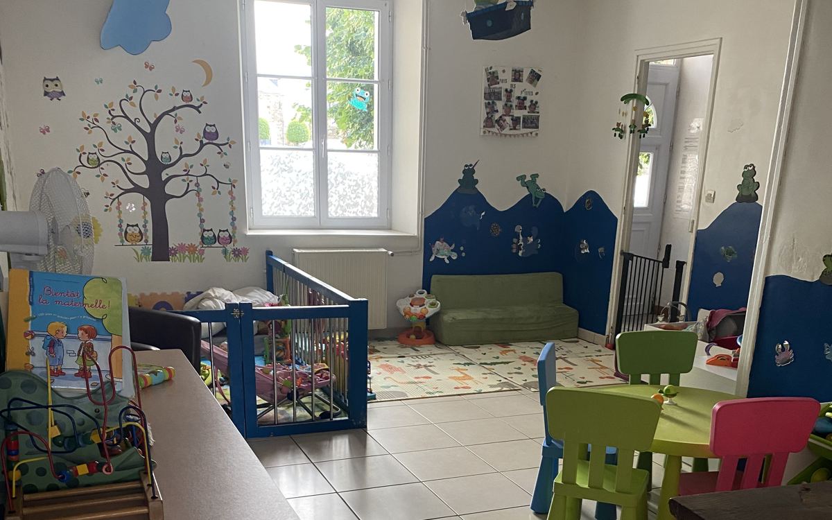 Image MAM 2 agrandie — Salle de vie de la MAM avec espace bébés, coin repas et décor mural